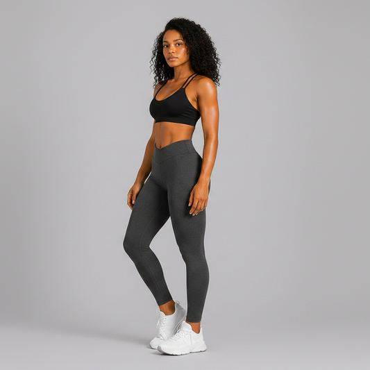 Woman wearing a black sports bra and gray leggings on a gray background