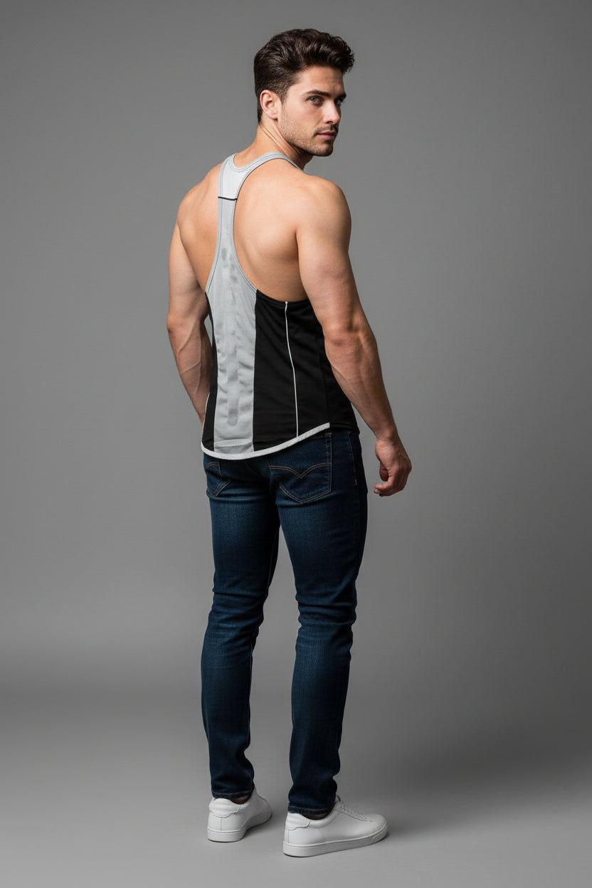 Man wearing a black and gray tank top with blue jeans on a gray background