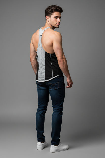 Man wearing a black and gray tank top with blue jeans on a gray background