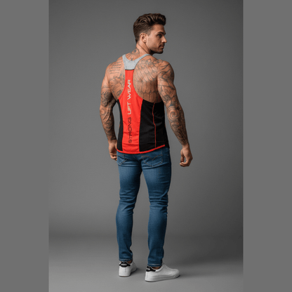 Man wearing a red and black athletic tank top with blue jeans on a gray background