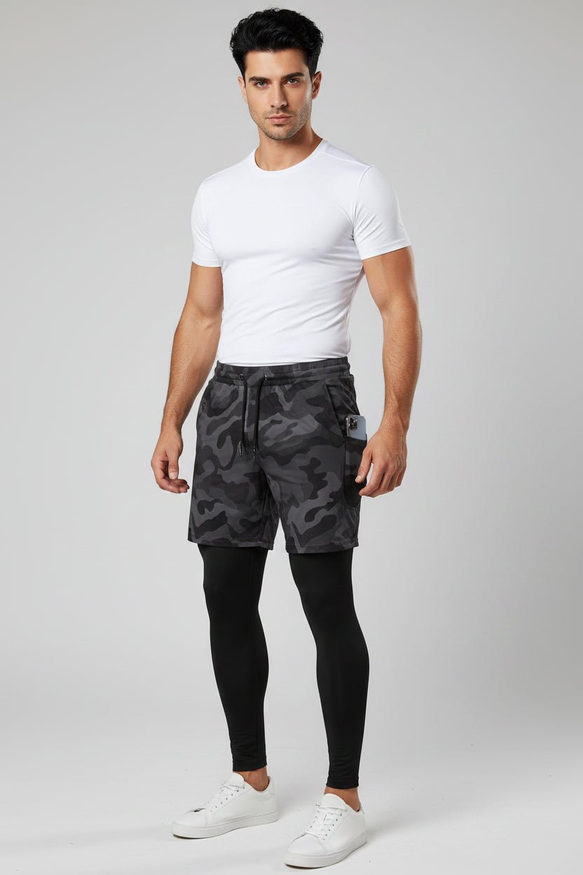 Man wearing a white t-shirt, black camouflage shorts, and black leggings on a light gray background