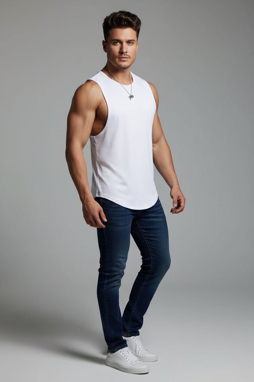 Man wearing a white tank top and blue jeans on a gray background