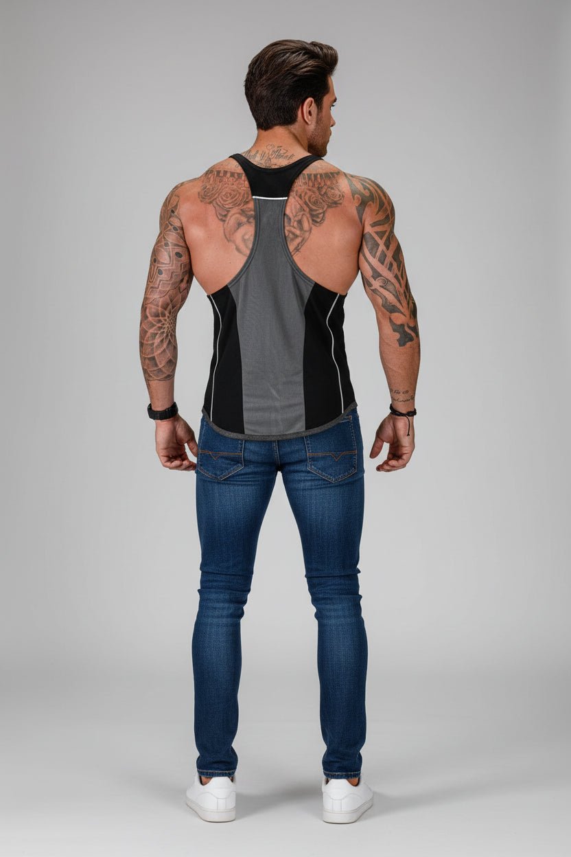 Man wearing a black and gray tank top and blue jeans on a gray background