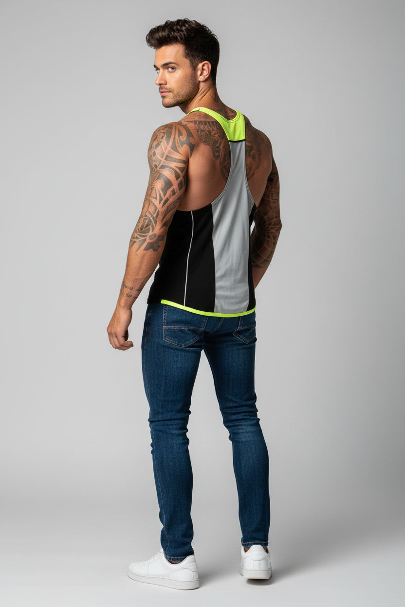 Man wearing a sleeveless black and gray top with green accents and blue jeans on a gray background