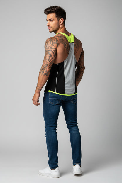 Man wearing a sleeveless black and gray top with green accents and blue jeans on a gray background
