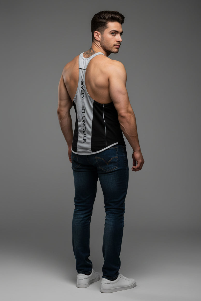 Man wearing a tank top and dark jeans on a gray background