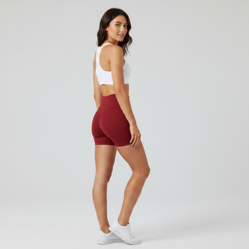 Woman wearing a white sports bra and maroon shorts on a plain background - Aresfit